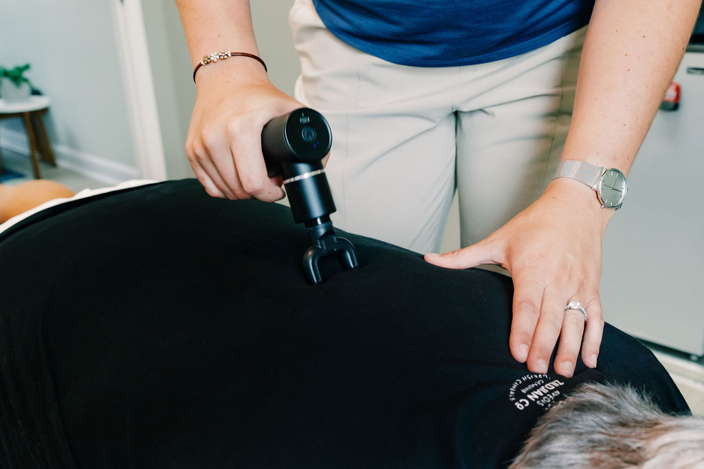 Dr Dalton Tolliver using a handheld massage instrument to assist with chiropractic care through muscle release therapy to assist with joint pain