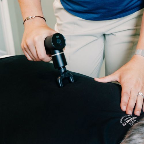 Dr Dalton Tolliver using a handheld massage instrument to assist with chiropractic care through muscle release therapy to assist with joint pain